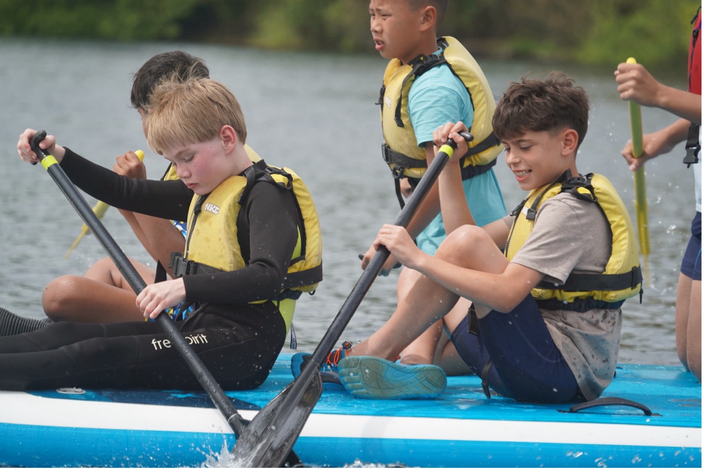 Young people on a Mega SUP paddling through a lake